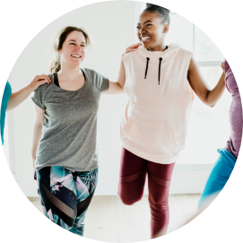 Ein Frauen-Kurs wo sich alle gegenseitig in einem Kreis an die Schultern fassen und sich dabei auf einem Bein dehnen.