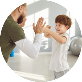 Ein Junge ca. 5 Jahre alt und sein Trainer ca. 42 Jahre alt die zusammen Fausthiebe üben im Kursraum.