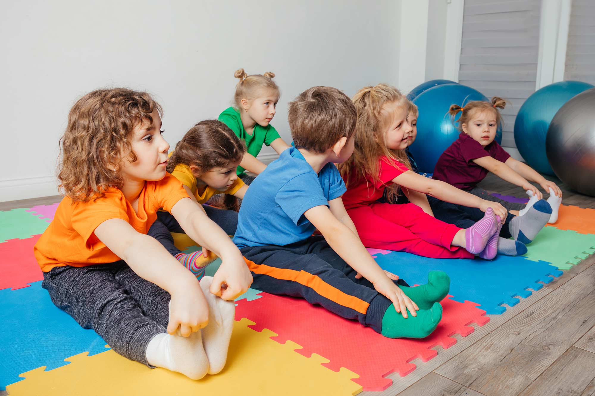 Kinder Kurs gruppe die sich auf den Boden auf turnmatten die Beine dehnen.