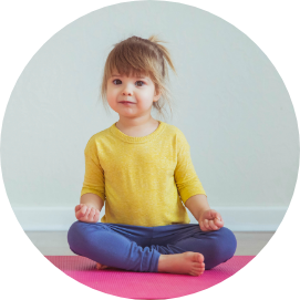 Mädchen ca. 4 Jahre alt in lockerer Sportbekleidung im Schneidersitz auf einer Yogamatte.